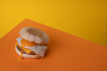 Fried Egg and Sausage Breakfast Muffin on a Funky Yellow and Orange Background