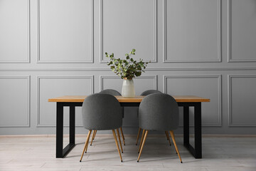 Soft chairs, table and vase with eucalyptus branches in stylish dining room