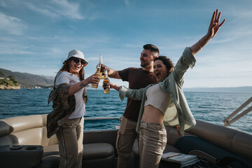 Group of cheerful friends enjoying a boat ride on a lake, toasting with beer and celebrating...