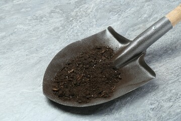 Metal shovel with fertile soil on gray textured surface