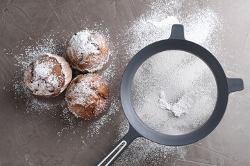 Naklejka premium Sieve with sugar powder and muffins on grey textured table, flat lay