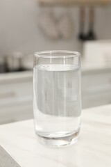 Glass with clear water on white marble table in kitchen