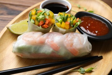 Tasty spring rolls and sauces on wooden plate, closeup