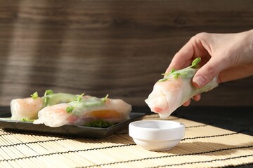 Woman dipping delicious spring roll into sauce at table, closeup
