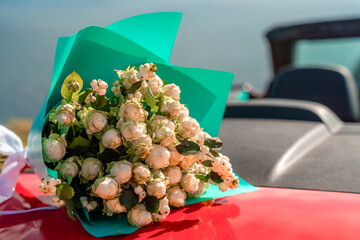 A bouquet of flowers is sitting on the hood of a red car. The flowers are white and red, and they...