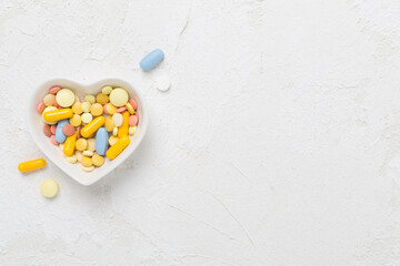 Medicines in heart-shaped bowl on concrete background, top view