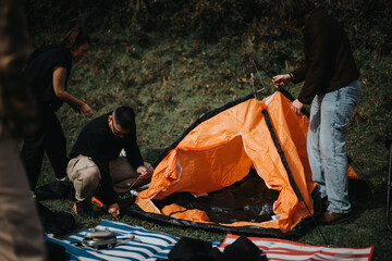 Group of friends working together to set up an orange tent on a camping trip in nature