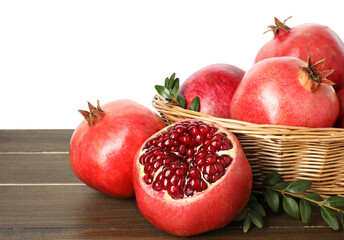Fresh pomegranates in wicker basket and green leaves on wooden table against white background