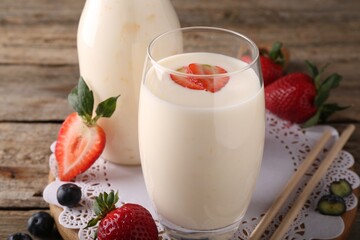 Tasty yogurt in glass, straws and berries on wooden table, closeup