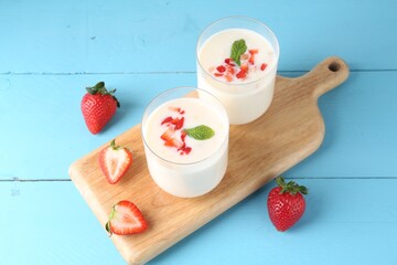 Tasty yogurt in glasses and strawberries on light blue wooden table