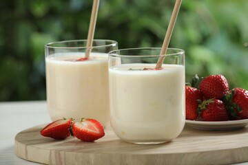 Tasty yogurt in glasses and strawberries on table outdoors, closeup