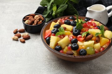 Delicious fruit salad in bowl, nuts and fresh mint on grey table. Space for text