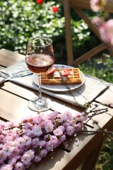 Delicious Belgian waffle with fresh strawberries and wine served on table in spring garden