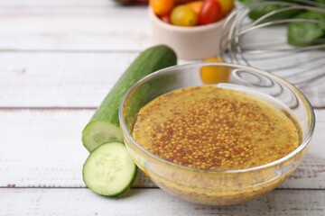 Tasty vinegar based sauce (Vinaigrette) in bowl and cucumber on wooden rustic table, closeup. Space for text