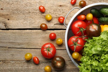 Fresh vegetables in colander on wooden table, flat lay. Space for text