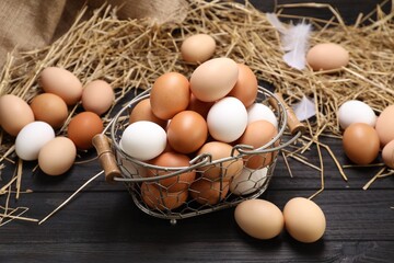 Fresh chicken eggs and dried straw on black wooden table