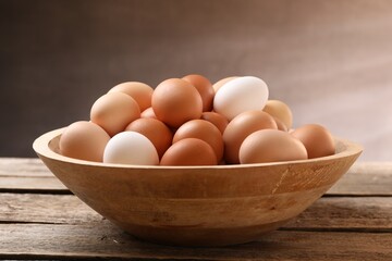 Chicken eggs in bowl on wooden table, closeup