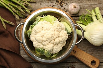 Metal colander with cauliflower, fennel and asparagus on wooden table, flat lay