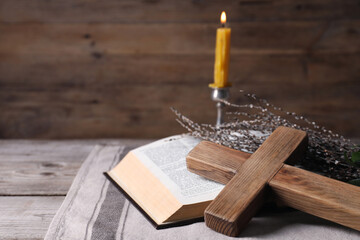 Cross, Bible, willow branches and burning candle on wooden table, space for text