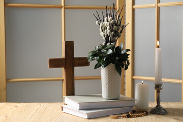 Cross, burning candles, books, rosary beads and bouquet with willow branches on wooden table