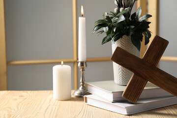 Cross, burning candles, books and bouquet with willow branches on wooden table