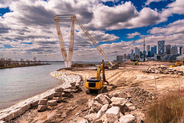 heavy machinery reshaping a river mouth with a city skyline, white clouds and blue sky in...