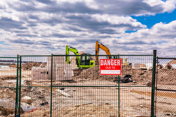 Fototapeta na wymiar danger due to construction sign on security fencing with heavy equipment and concrete pipes in the background with white clouds and blue sky room for text shot toronto portlands development