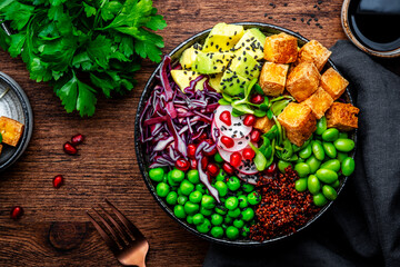 Vegan Buddha Bowl for balanced diet with tofu, quinoa, vegetables and legumes. Wooden table background, top view