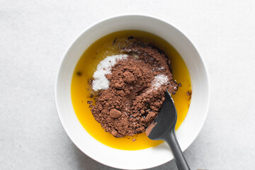 overhead view of melted butter white sugar and brown sugar cocoa powder in a white bowl, the...