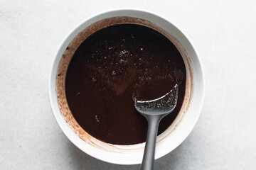 overhead view of melted butter white sugar and brown sugar cocoa powder in a white bowl, the...