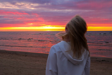 A girl admires the sunset on the sea. Hair blowing in the wind