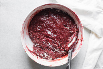 flour being mixed into red velvet brownie batter in a white mixing bowl, overhead view of red...