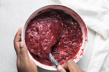flour being mixed into red velvet brownie batter in a white mixing bowl, overhead view of red...