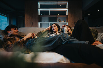 A young couple enjoys a lazy evening on the sofa, browsing on their phones in a comfortable living...