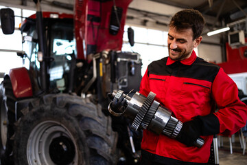 Professional mechanic repairing tractor transmission inside workshop.