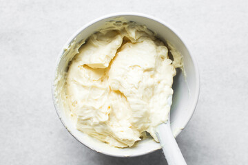Top view of cream buttercream in a white mixing bowl, silky smooth american buttercream in a...