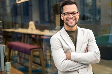 Beautiful cheerful man smiling at camera with crossed arms standing outside at a Cafe.