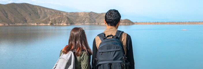 A loving traveling couple with backpacks looking at the lake. stock photo
