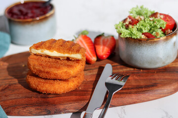 Fresh made and cutted fried camembert cheese with a side of fresh salad on wooden plate, white...