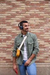 Vertical of young adult Caucasian stylish man smiling with wireless headphones holding cell phone...