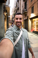 Vertical young happy Caucasian man taking smiling selfie on Madrid touristic city street in...