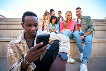 Serious black guy using smart phone. African American man holding cell outdoor with friends...