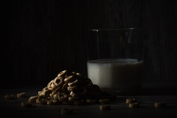 a pile of cereals next to a translucid glass with some milk, in a dark food style photopraphy