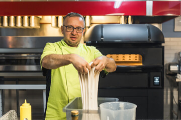 chef with glasses and uniform kneading the dough in the bakery kitchen. High quality photo
