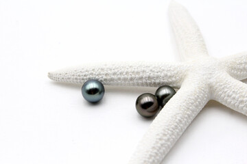 Expensive and luxurious Tahiti black pearls near a white starfish on white background, ready to be...
