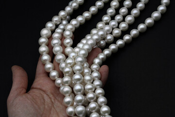 Chinese round freshwater white pearls on strands ready to become a necklace, some of the favorite materials for jewelry held in a jeweler's hand. Lustrous nacre forms an organic gem.