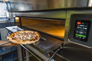 putting pizza with mushrooms and meat in an electric oven, restaurant kitchen. High quality photo