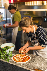 vertical shot of a woman cook adding ingredients to pizza at the bakery. High quality photo