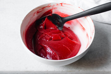 Folding Red velvet batter in a white mixing bowl, process of making red velvet madeleines, thick...