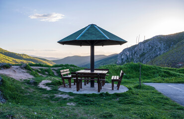 Table in the mountain resting place with a canopy from the rain and benches, a place to relax in nature. Resting place in Nature Park Sicevo Canyon. A wooden summer house with a green roof.